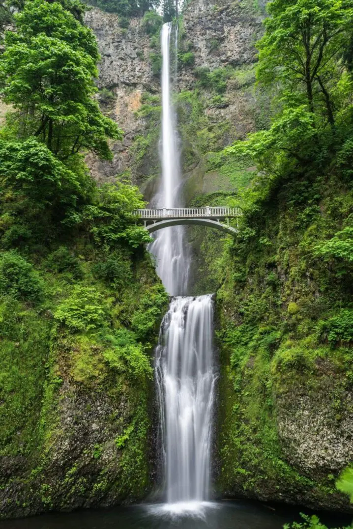 A tall waterfall cascading over rocky cliffs with a bridge crossing midway.